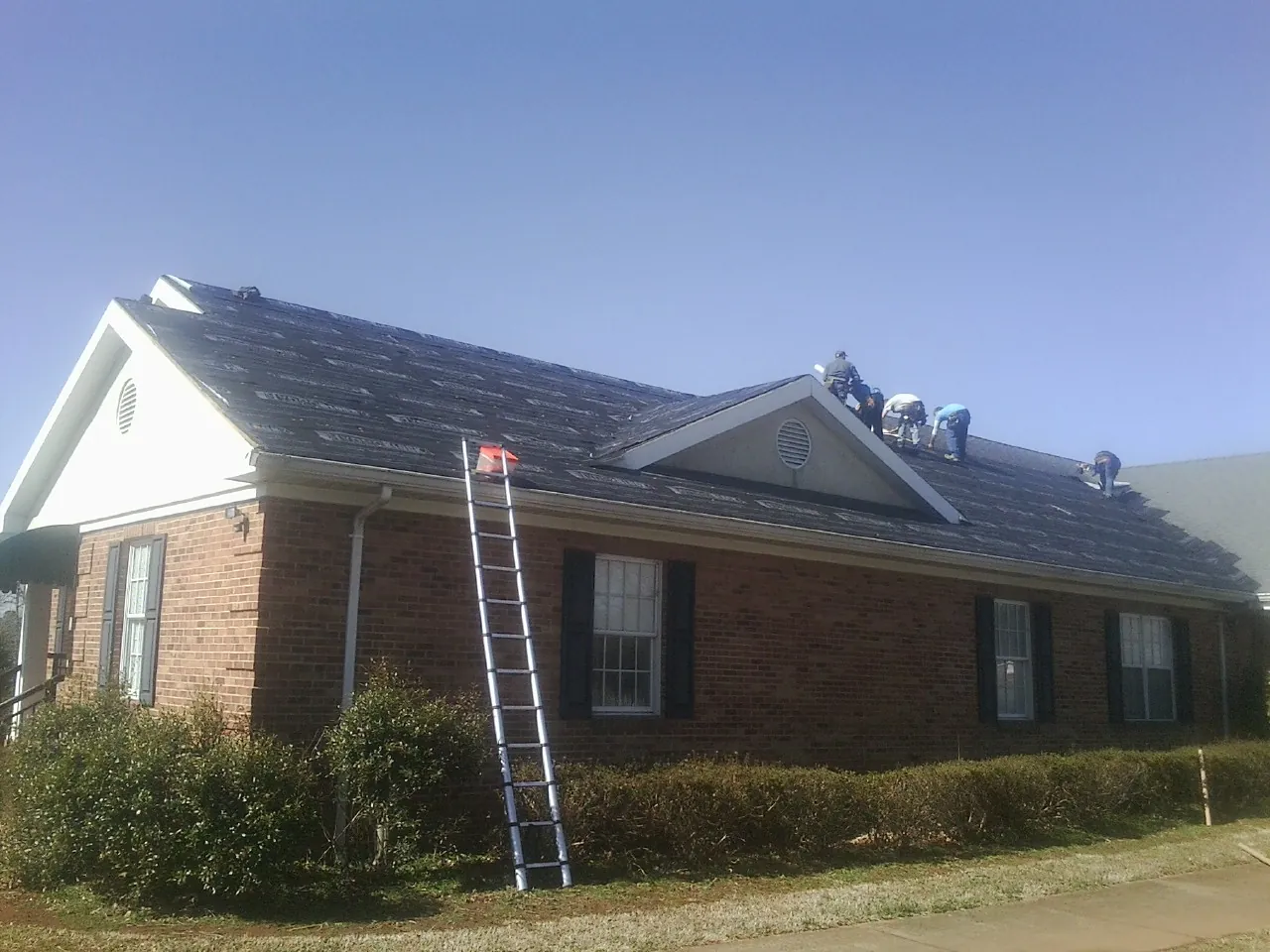 Crew tearing shingles off a brick ranch roof with a ladder set — Emergency Roof Repair work by our crew in Mountain Lakes