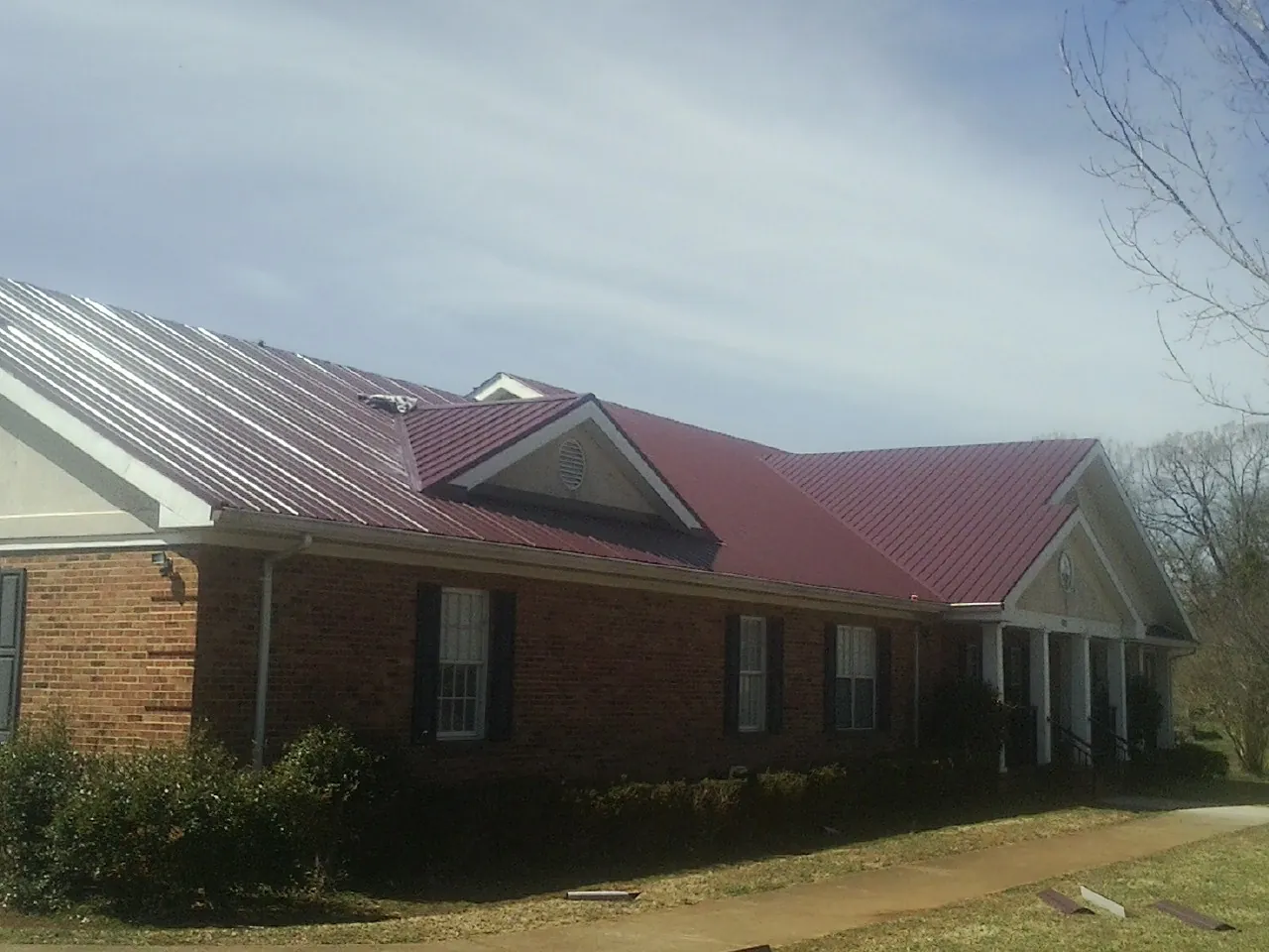 Red metal roof with gabled entries on a long brick building, from a Hail Damage Roof Repair job in Mountain Lakes