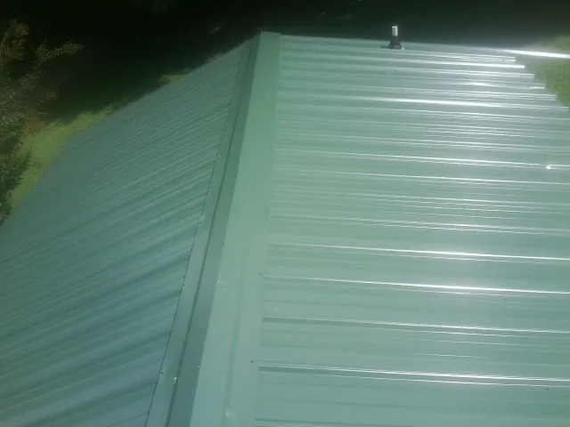 New green metal panels meeting at the ridge of a roof — Flat Roof Repair work by our crew in Mountain Lakes