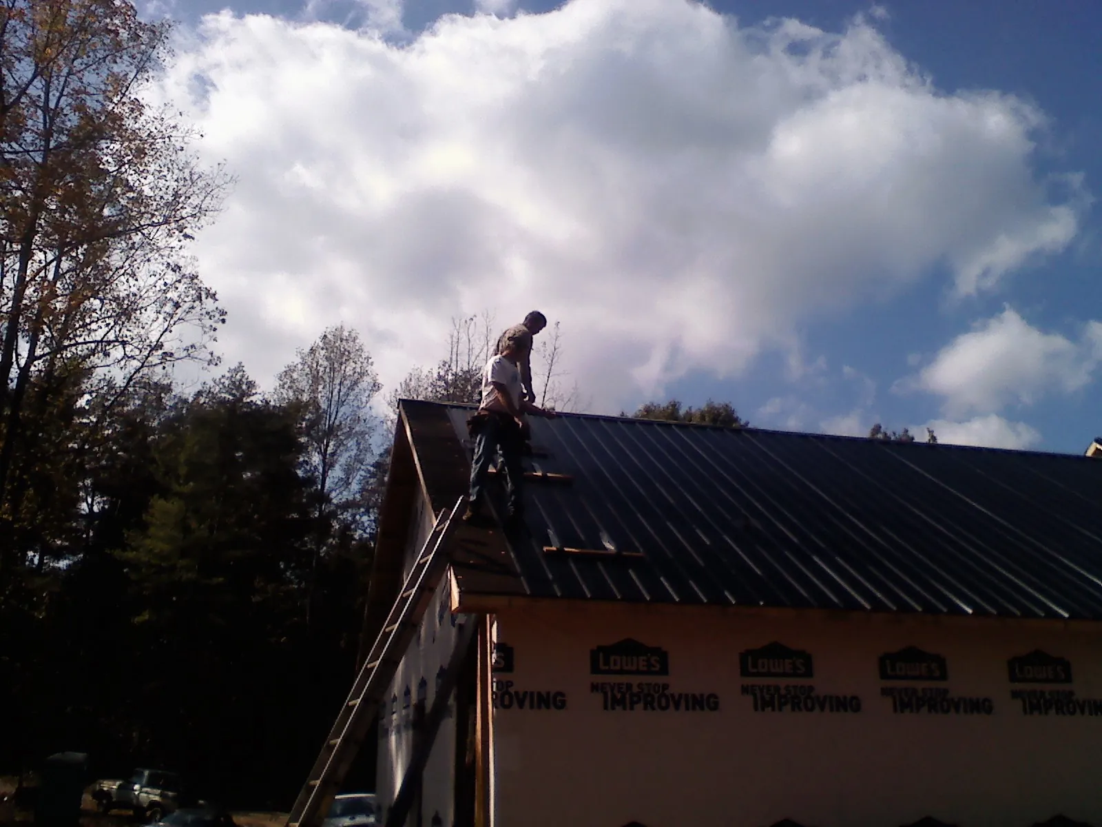 Roofer fastening dark metal panels high against a cloudy sky, from a Roof Inspection job in Mountain Lakes