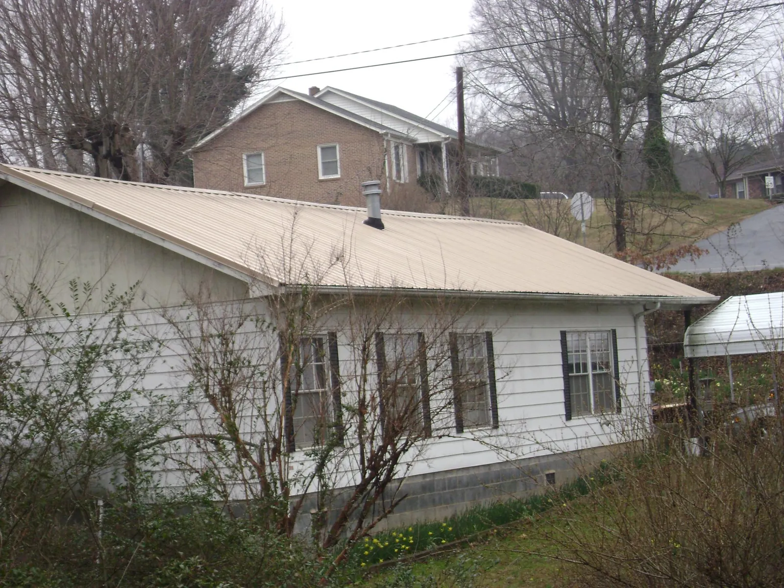 Tan metal roof on a white sided house set into a hillside — Commercial Roofing by Roofing Brothers in Mountain Lakes