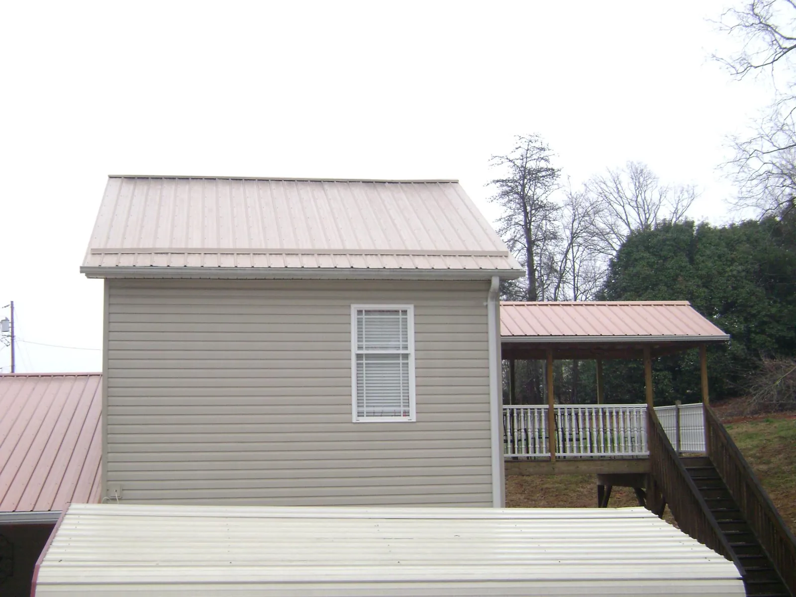 Tan metal roofs on a two story addition and attached porch, from a Roof Replacement job in Mountain Lakes